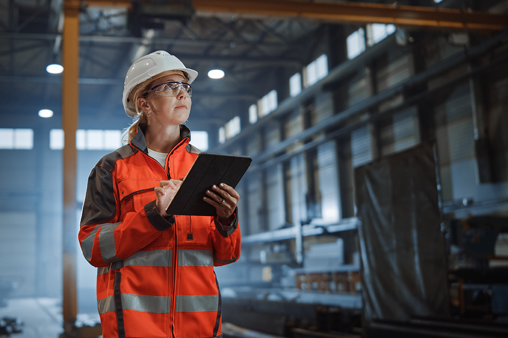 Successful Female Industrial Specialist Walking in a Metal Manufacture Warehouse.